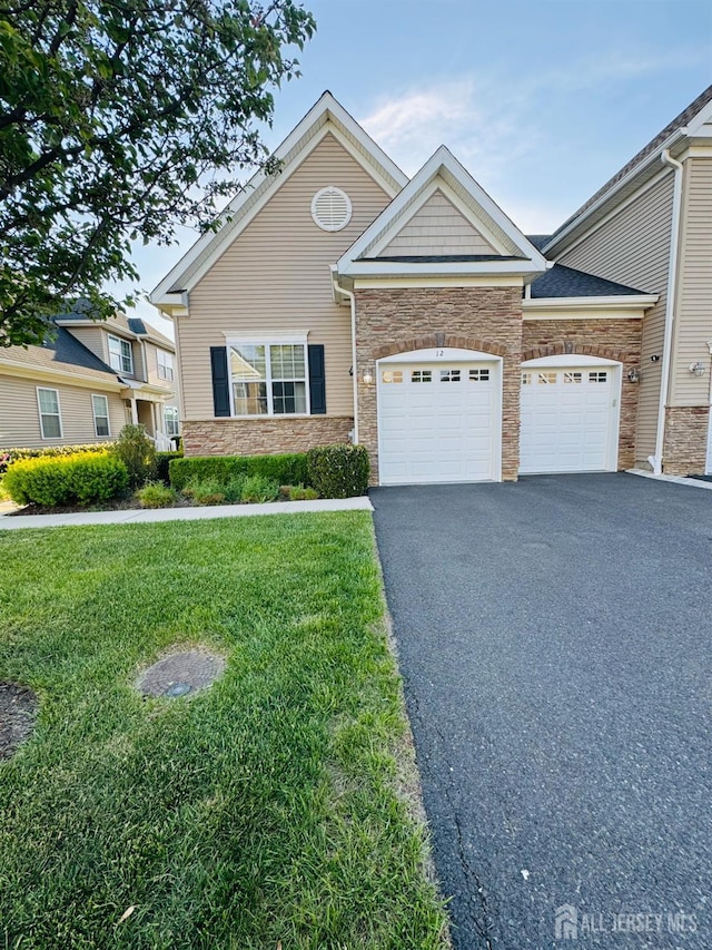 view of front of house with a garage, a front lawn, driveway, and stone siding