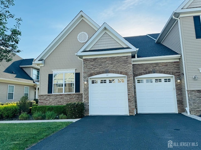 view of front of house featuring an attached garage, aphalt driveway, and stone siding