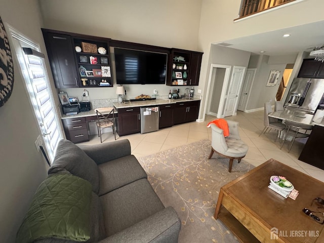 living area with indoor wet bar, baseboards, light tile patterned floors, and a towering ceiling