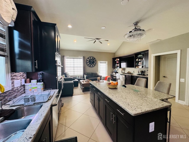 kitchen with a kitchen island, open floor plan, dark cabinets, a ceiling fan, and light tile patterned floors