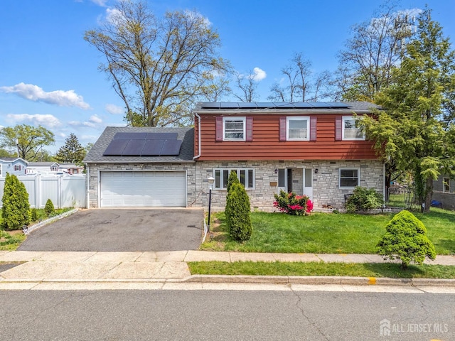 colonial inspired home featuring roof mounted solar panels, stone siding, driveway, and a garage