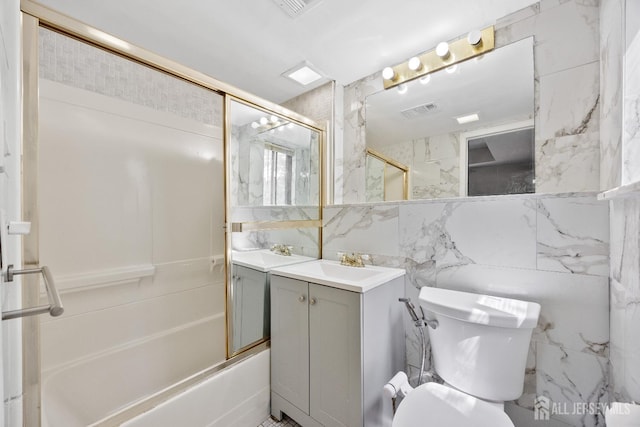bathroom featuring toilet, vanity, tile walls, and bath / shower combo with glass door