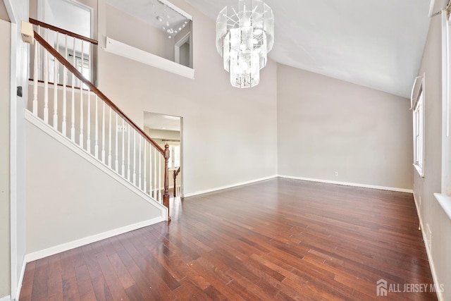 unfurnished living room featuring stairs, wood finished floors, a chandelier, baseboards, and a towering ceiling
