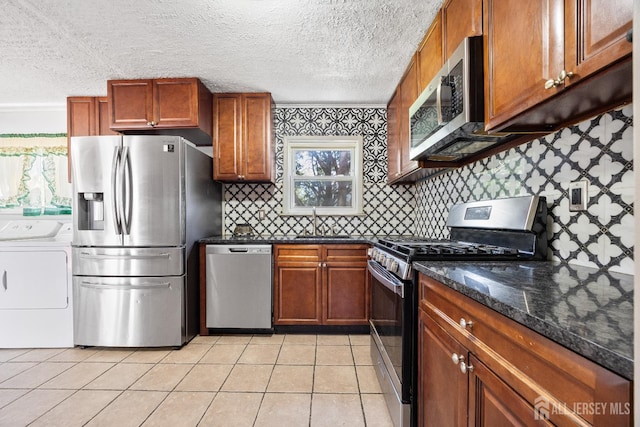 kitchen with appliances with stainless steel finishes, independent washer and dryer, a sink, brown cabinetry, and backsplash