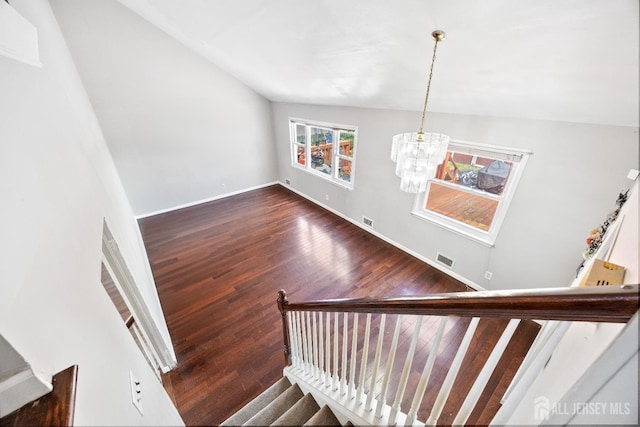 stairway featuring a chandelier, wood finished floors, baseboards, and lofted ceiling