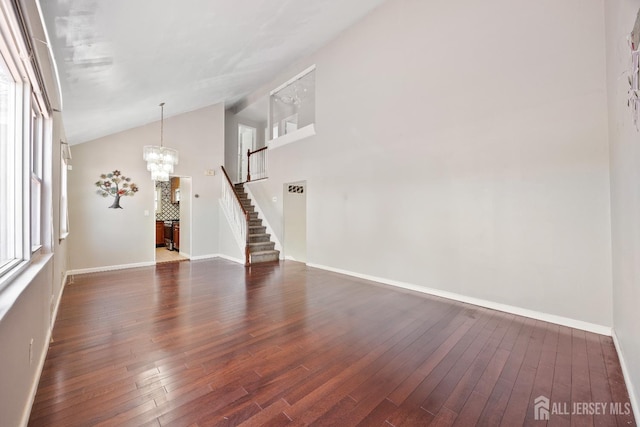 unfurnished living room with a chandelier, dark wood-style floors, stairway, baseboards, and high vaulted ceiling