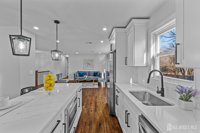 kitchen with pendant lighting, dark wood-type flooring, light stone counters, sink, and white cabinetry