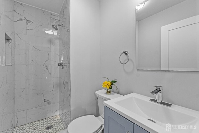 bathroom featuring a tile shower, vanity, and toilet