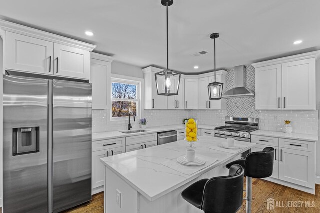 kitchen with wall chimney exhaust hood, pendant lighting, white cabinetry, appliances with stainless steel finishes, and sink