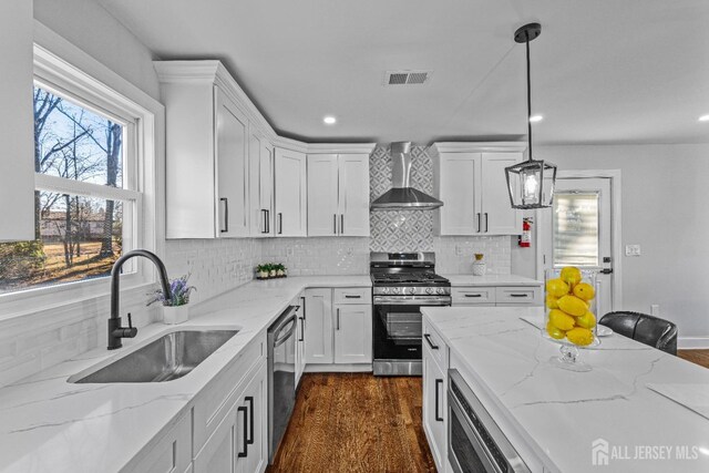 kitchen featuring stainless steel appliances, white cabinets, wall chimney range hood, and pendant lighting