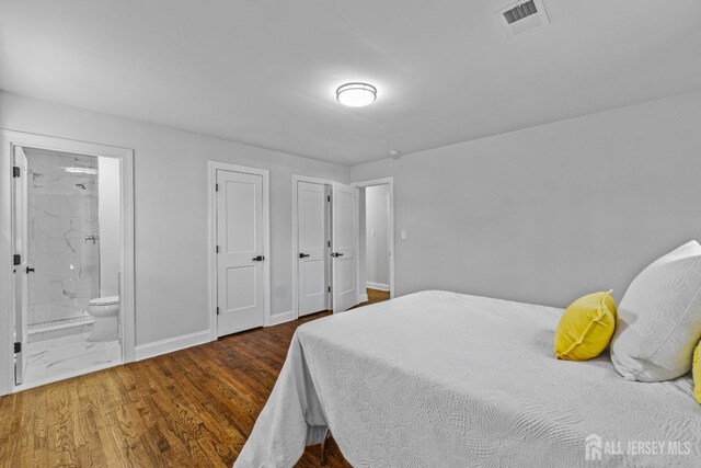 bedroom featuring ensuite bath, dark wood-type flooring, and multiple closets