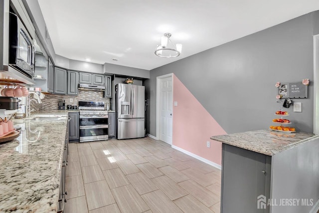 kitchen with a sink, stainless steel appliances, decorative backsplash, under cabinet range hood, and gray cabinetry