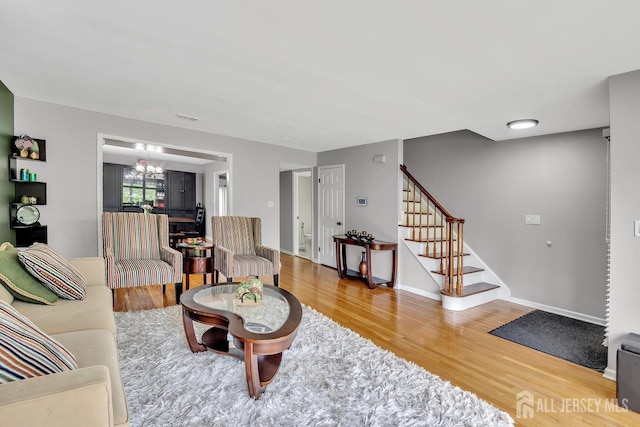 living room featuring stairway, an inviting chandelier, wood finished floors, and visible vents