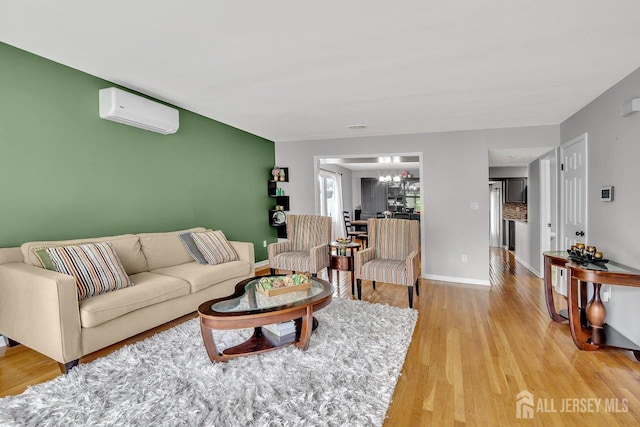 living area with an AC wall unit, baseboards, an inviting chandelier, and light wood-style flooring