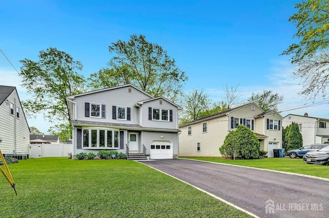 view of front of house featuring a front lawn, fence, entry steps, an attached garage, and driveway