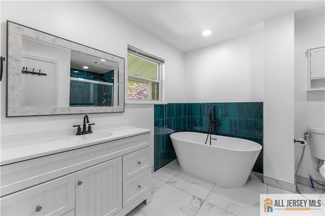 full bathroom featuring marble finish flooring, vanity, toilet, a freestanding tub, and wainscoting