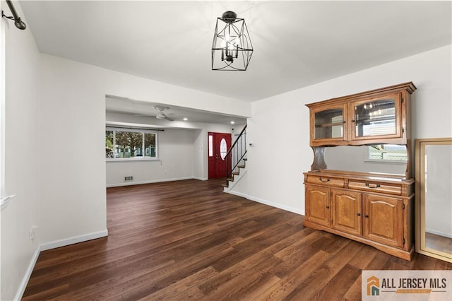 unfurnished dining area with dark wood-type flooring, stairway, baseboards, and ceiling fan