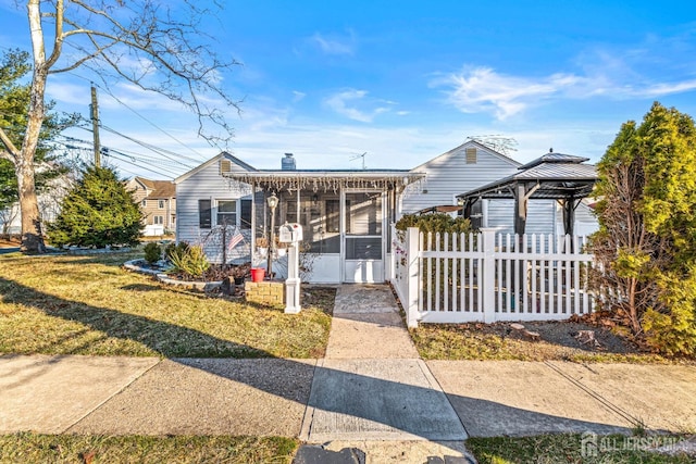 view of front of house featuring fence, a sunroom, a chimney, a gazebo, and a front lawn