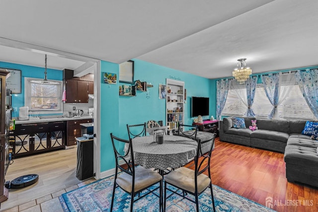 dining area with baseboards, an inviting chandelier, light wood-style flooring, and a healthy amount of sunlight