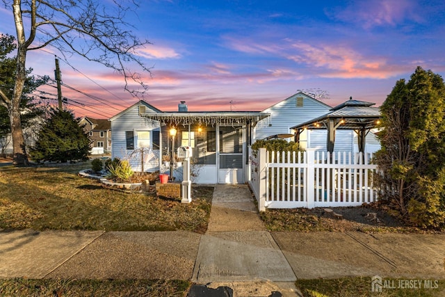 view of front of house with a gazebo, fence, a sunroom, and a chimney