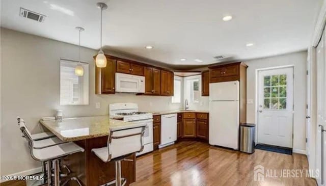 106 Manalapan Rd, Spotswood, NJ 08884 - kitchen featuring white appliances, wood finished floors, a peninsula, decorative light fixtures, and a kitchen breakfast bar