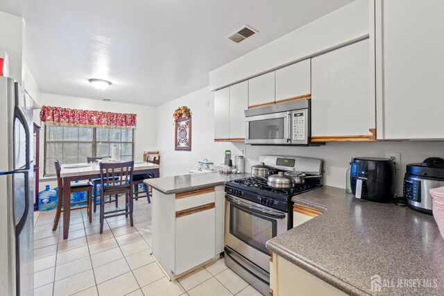 kitchen with white cabinets, light tile patterned floors, stainless steel appliances, and kitchen peninsula