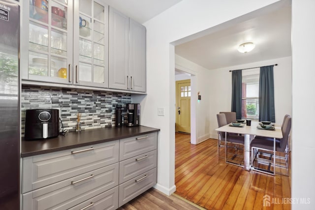 373 Rushmore Ave, Piscataway, NJ 08854 - kitchen featuring light wood-style floors, dark countertops, decorative backsplash, freestanding refrigerator, and glass insert cabinets