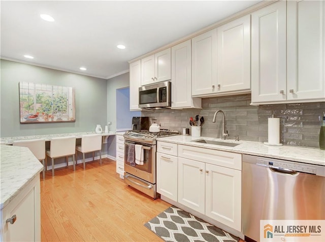 kitchen featuring ornamental molding, a sink, backsplash, stainless steel appliances, and light wood-style floors