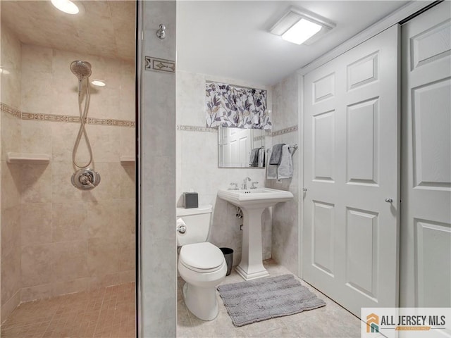 bathroom featuring a sink, a tile shower, toilet, and tile walls