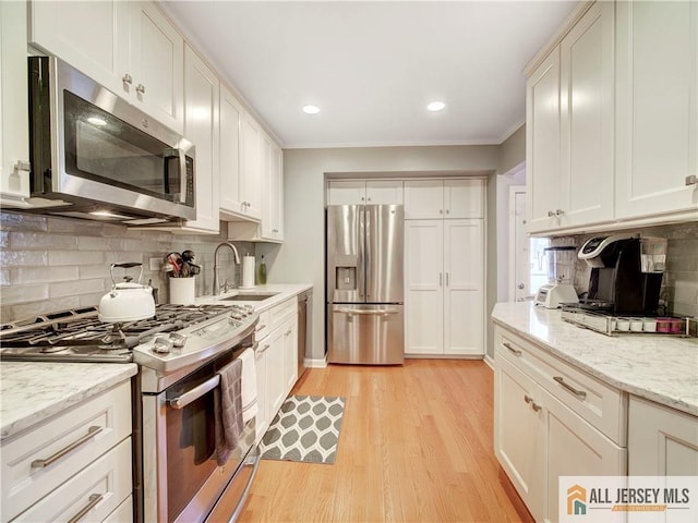 kitchen featuring light wood-style flooring, a sink, tasteful backsplash, appliances with stainless steel finishes, and white cabinets