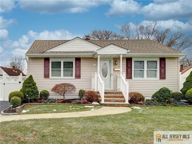 bungalow-style home with a shingled roof, a front yard, and fence