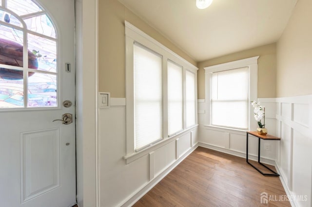 doorway to outside with a decorative wall, light wood finished floors, and wainscoting