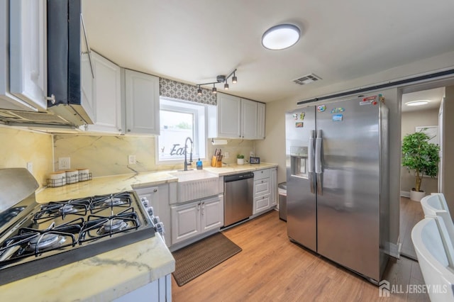 kitchen with light wood finished floors, a sink, stainless steel appliances, visible vents, and white cabinets