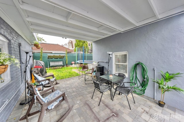 view of patio with fence, outdoor dining space, and a trampoline