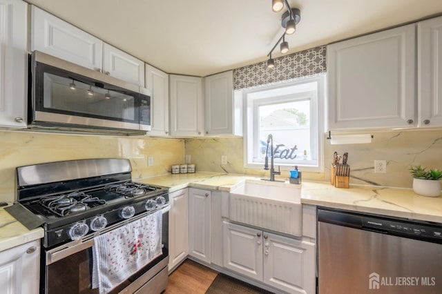 kitchen featuring light stone countertops, a sink, stainless steel appliances, track lighting, and white cabinetry