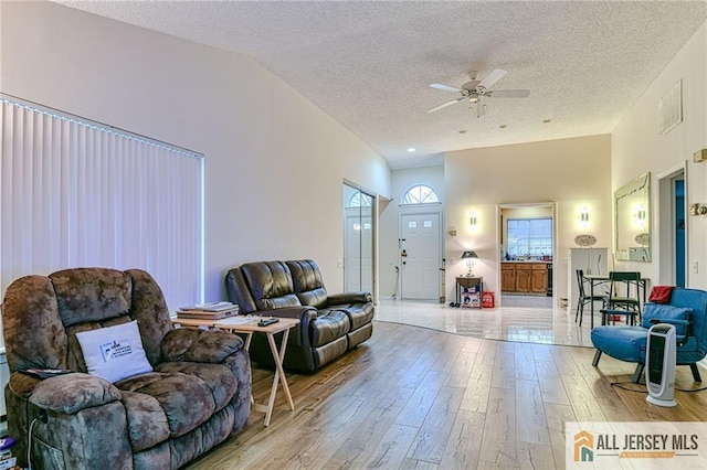 living room with ceiling fan, lofted ceiling, a textured ceiling, and light hardwood / wood-style flooring