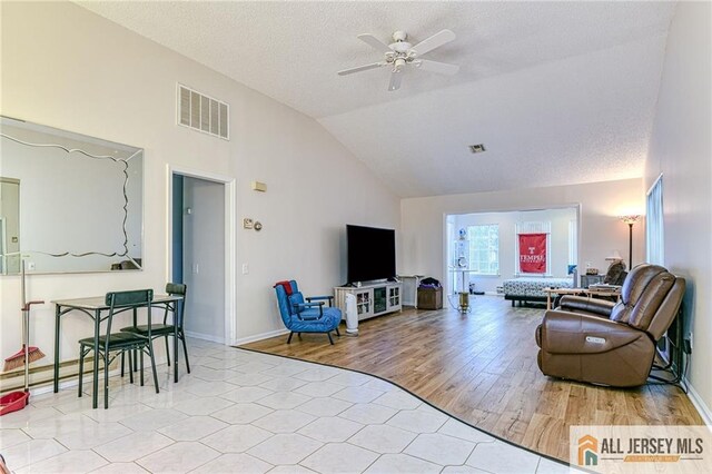 living room featuring ceiling fan, vaulted ceiling, a textured ceiling, and light hardwood / wood-style flooring