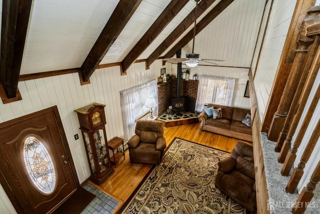 living room featuring vaulted ceiling with beams, wood walls, a wood stove, wood finished floors, and a ceiling fan