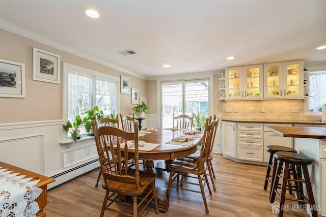 dining room with light wood-type flooring, visible vents, a wainscoted wall, ornamental molding, and baseboard heating