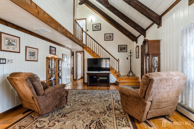 living area featuring a baseboard heating unit, stairway, beamed ceiling, and wood finished floors