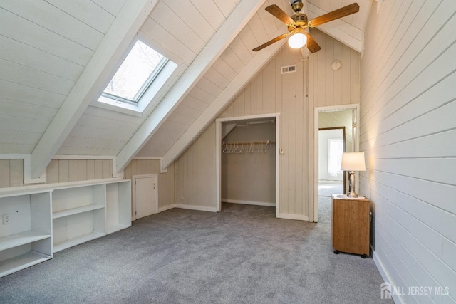 additional living space with visible vents, lofted ceiling with skylight, wood walls, carpet flooring, and a ceiling fan