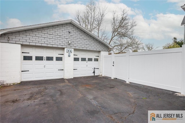 garage featuring fence and asphalt driveway