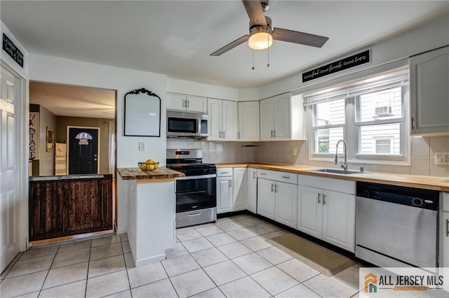 kitchen featuring appliances with stainless steel finishes, a sink, light tile patterned floors, decorative backsplash, and white cabinetry