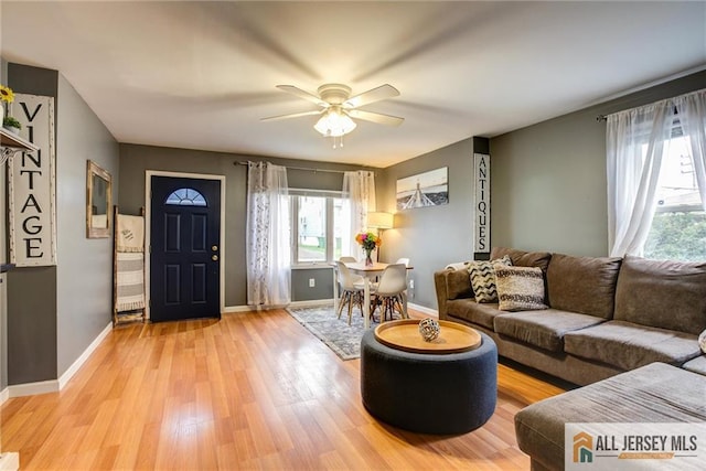 living area with a ceiling fan, light wood-style flooring, and baseboards