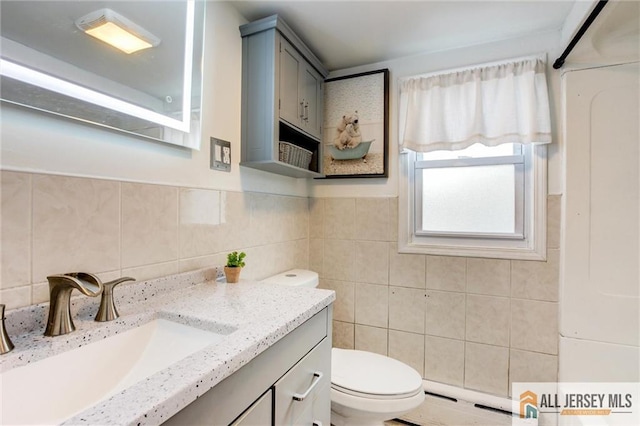 bathroom with a baseboard heating unit, tile walls, toilet, and vanity