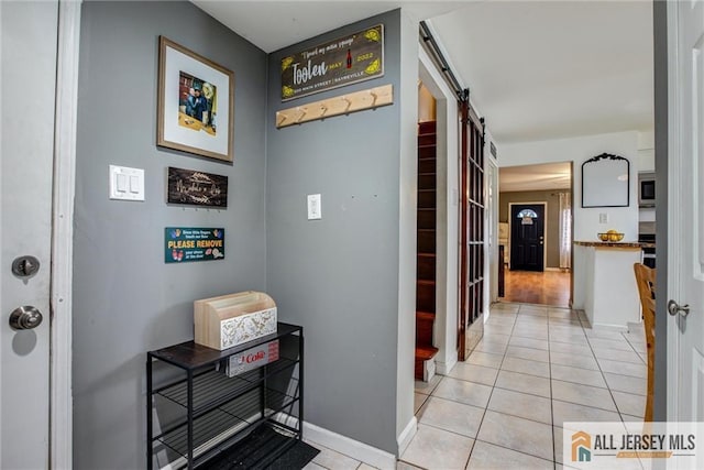 corridor with a barn door, light tile patterned flooring, and baseboards