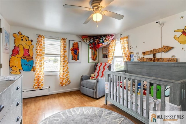 bedroom with baseboard heating, multiple windows, wood finished floors, and baseboards