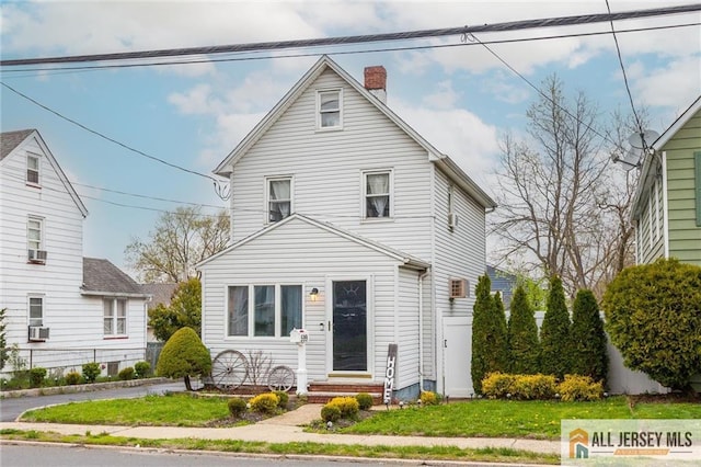 traditional style home featuring a chimney, entry steps, a front yard, and cooling unit