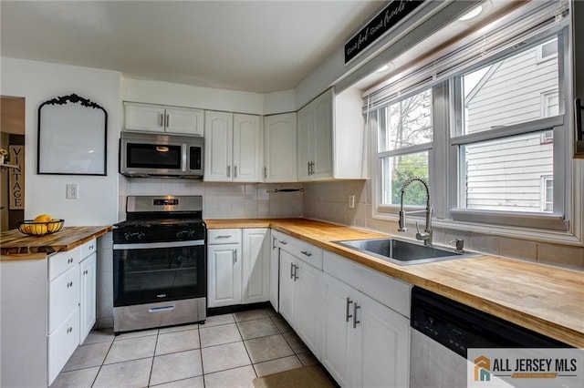 kitchen with butcher block countertops, appliances with stainless steel finishes, a sink, and white cabinetry