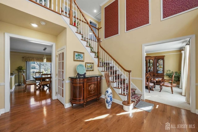 stairs with crown molding, wood-type flooring, a high ceiling, and french doors